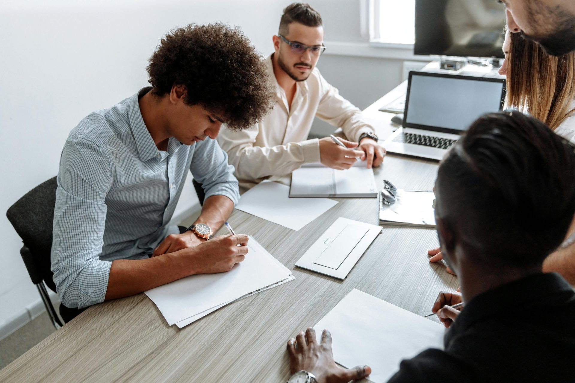 A multi-ethnic group working together at a desk with laptops and papers.
